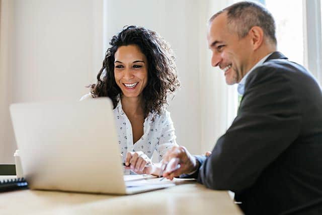 Two treasury professionals sitting at a table looking and smiling at a laptop computer