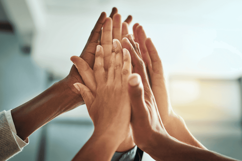 Multiple people's hands put together up in the air, representing the many parts of a treasury management system working together